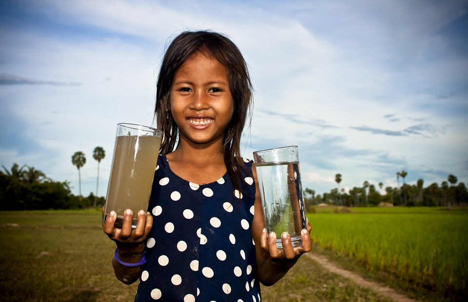 Ein Mädchen hat ein Glas dreckiges und ein Glas mit sauberem Trinkwasser in der Hand